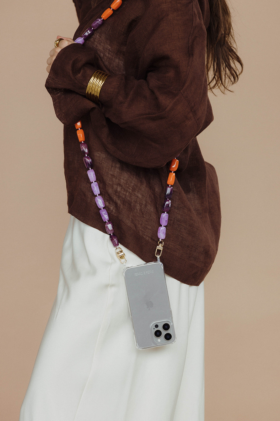 Close-up of a purple and orange bead phone chain attached to a phone in a clear case, worn against a brown linen top.