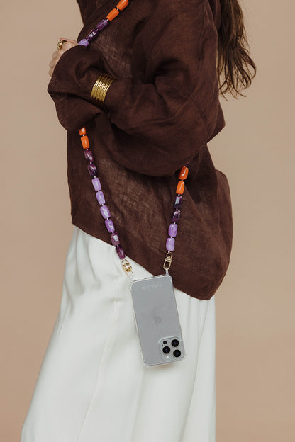Close-up of a purple and orange bead phone chain attached to a phone in a clear case, worn against a brown linen top.
