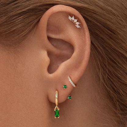 Juna Set worn on the ear, mixing a marquise crawler at the cartilage with emerald studs and a dangling emerald baguette hoop.