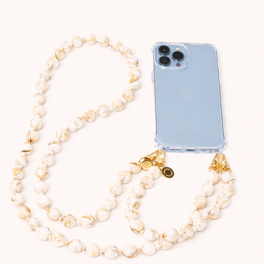 A cream and gold marbled bead phone chain attached to a clear phone case, with gold clasps and a charm, on a cream background.