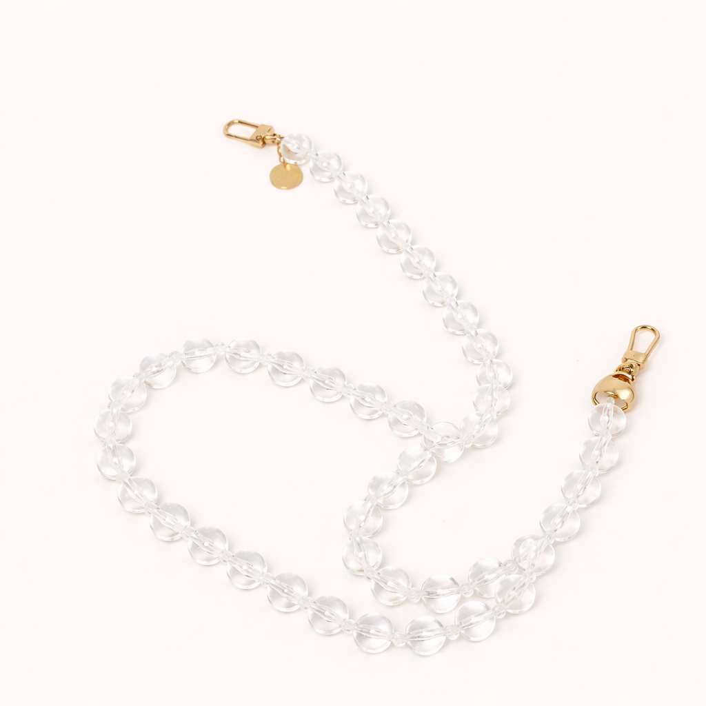 A coiled clear glass bead phone chain with gold clasps, shown on a cream background.