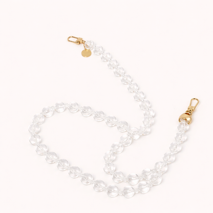 A coiled clear glass bead phone chain with gold clasps, shown on a cream background.
