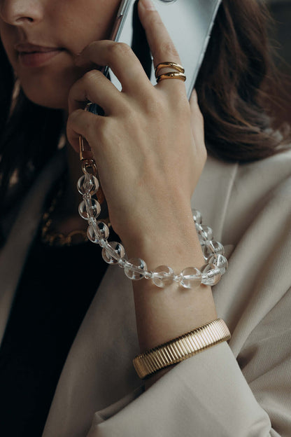 Close-up of a woman on the phone, wearing a clear glass bead bracelet on her wrist along with a ribbed gold bangle.