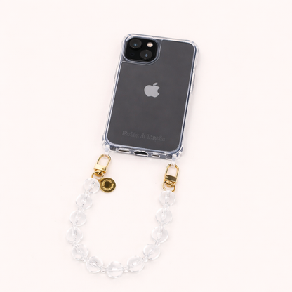 A clear phone case with a clear glass bead phone strap and a gold Folie à Trois charm, shown on a cream background.