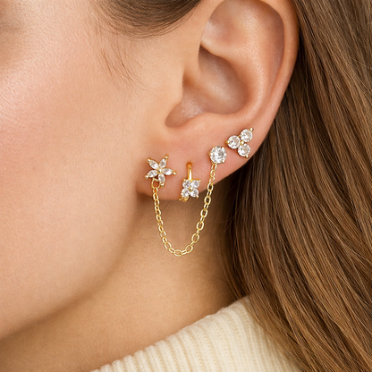 Worn along the ear, the Juno SET layers gold flower and star studs connected by a delicate draped chain.