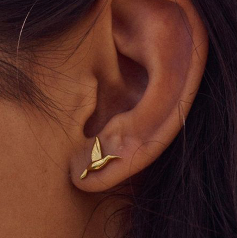Worn on a model's ear, the Kai EARRINGS hummingbird stud perches delicately along the earlobe in fine gold detail.