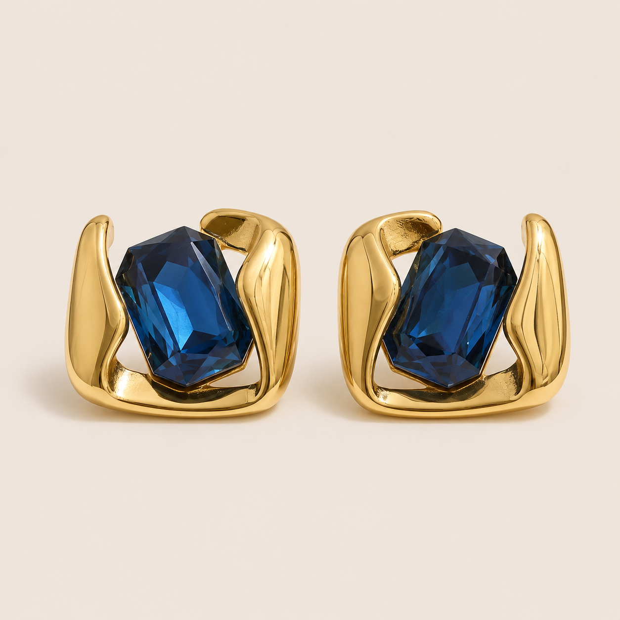 Gold sculptural stud earrings gripping a large emerald-cut blue stone in a swirled open frame — Folie à Trois Kaleidoscope EARRINGS