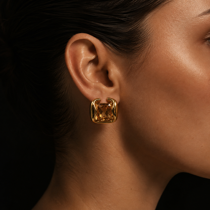 Close-up on the ear of the gold Kaleidoscope EARRINGS, a large champagne-toned stone gripped in a swirled sculptural frame.