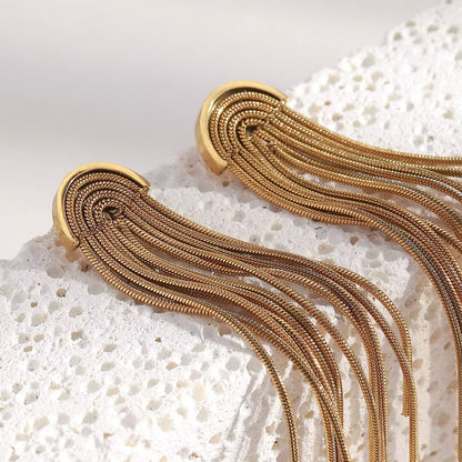 Close-up of Kiss and Tell Earrings in gold on a porous white stone, showing the fine chain fringe strands.