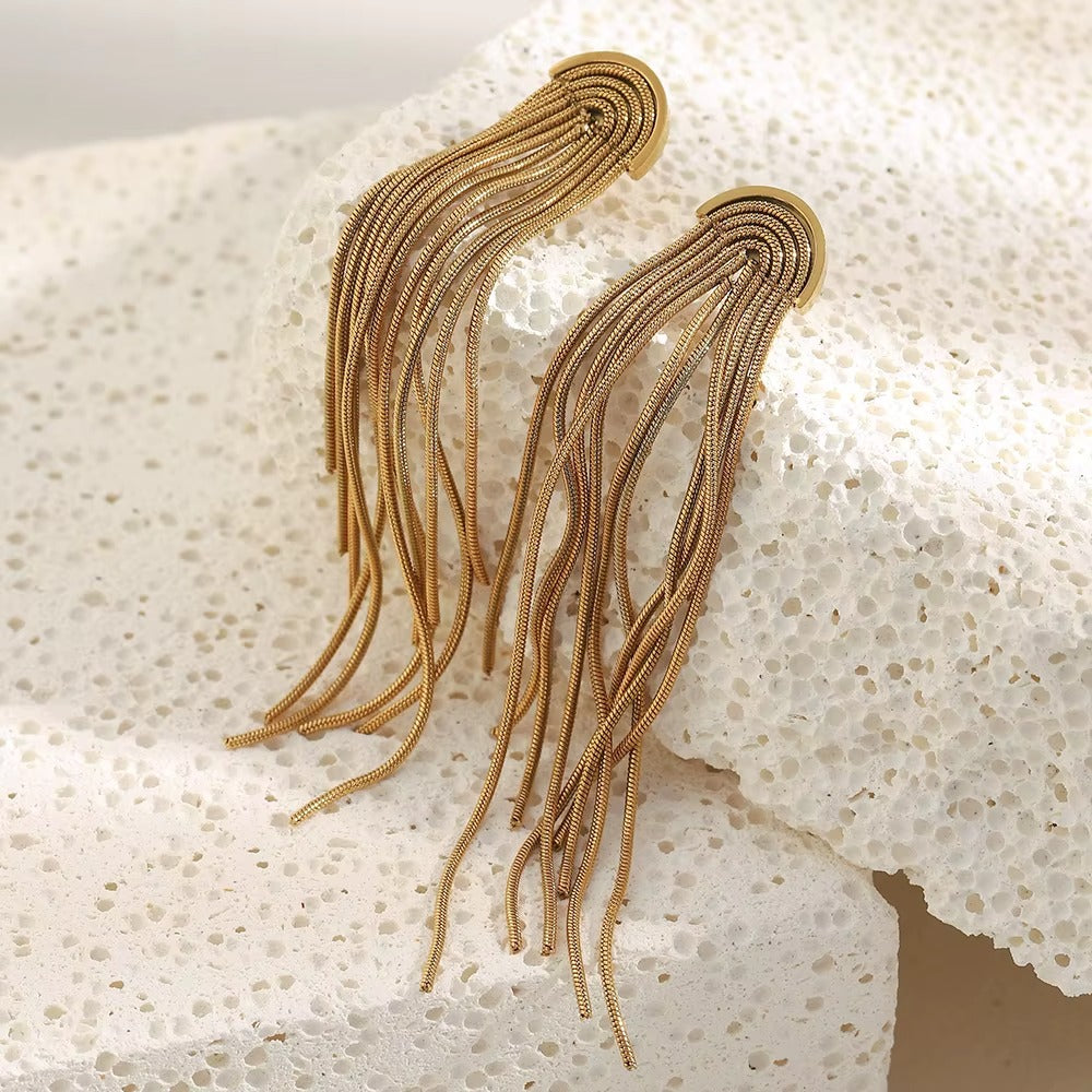 Kiss and Tell Earrings in gold resting on a white stone from another angle, chain fringe cascading down.