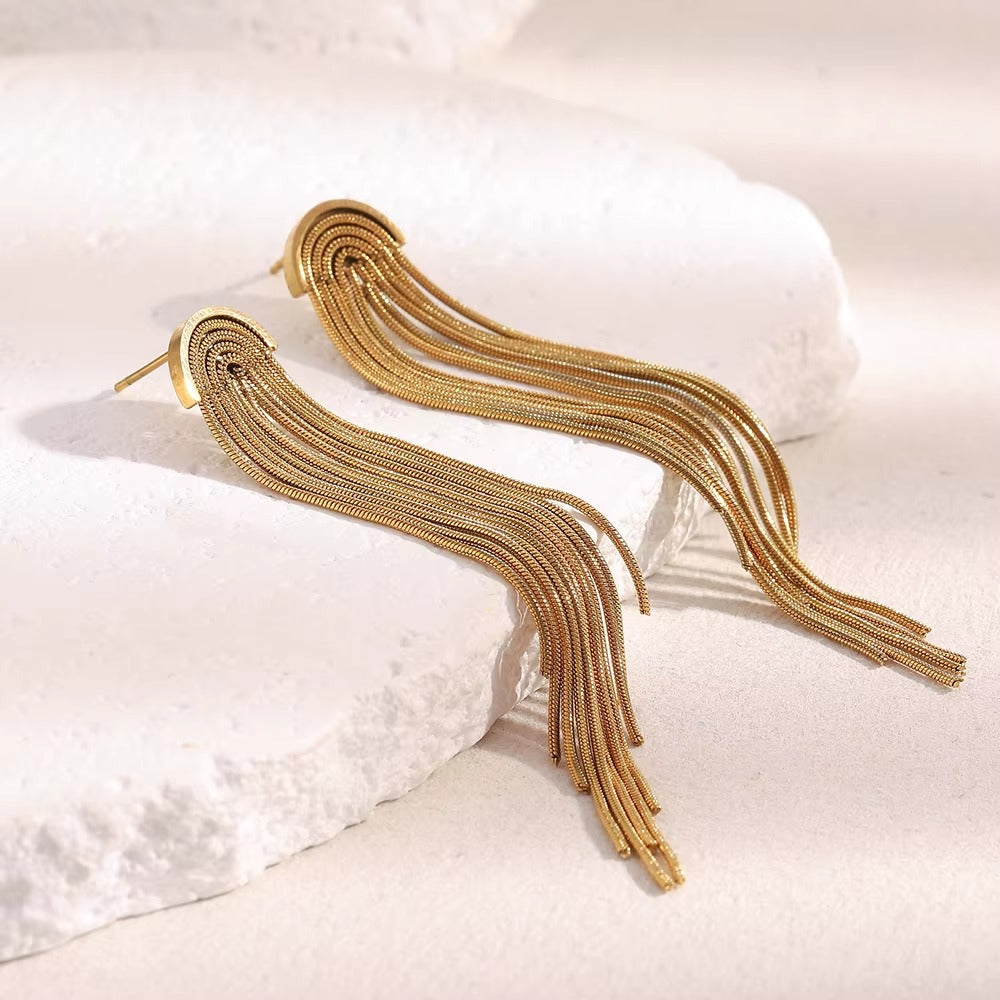 Kiss and Tell Earrings in gold laid side by side on white stone, both showing the long chain fringe design.