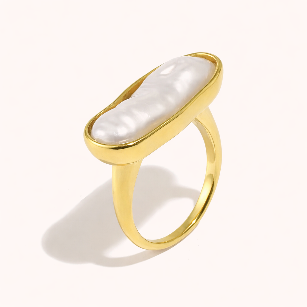 Gold ring set with an elongated baroque pearl in an oval bezel, shown at an angle on a cream backdrop — Folie à Trois La Mer RING.