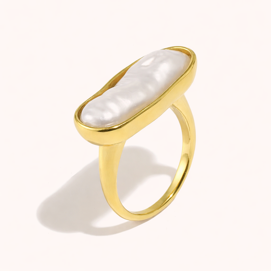 Gold ring set with an elongated baroque pearl in an oval bezel, shown at an angle on a cream backdrop — Folie à Trois La Mer RING.