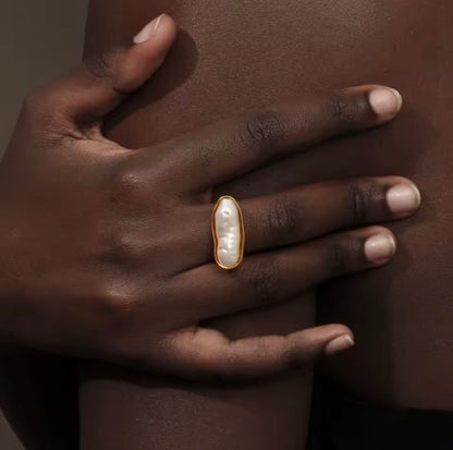 Close-up of a hand wearing the gold La Mer RING with its elongated baroque pearl, resting against bare skin.
