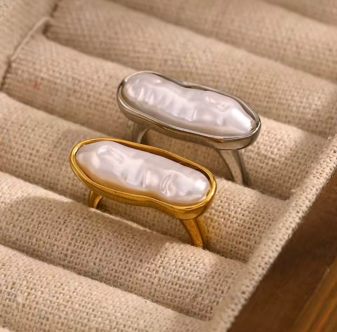Gold and silver La Mer RING styles displayed together in a linen-lined jewelry tray, each set with a baroque pearl.