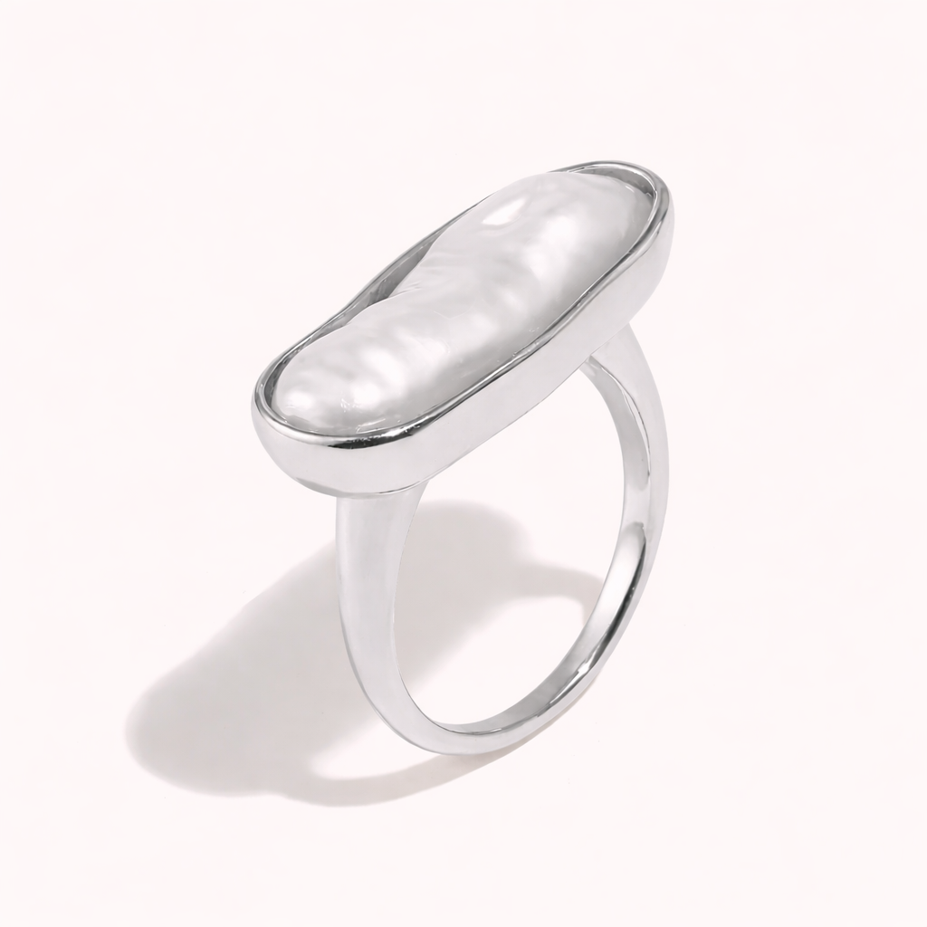 Silver ring set with an elongated baroque pearl in an oval bezel, shown at an angle on a cream backdrop — La Mer RING.