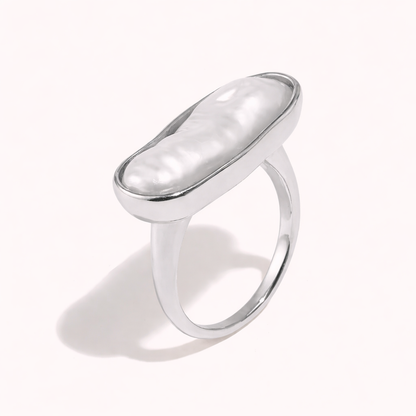 Silver ring set with an elongated baroque pearl in an oval bezel, shown at an angle on a cream backdrop — La Mer RING.