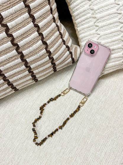 Brown and gold chip-bead Lagoon Stones SHORT PHONE STRAP attached to a pink phone case, resting on woven cushions.