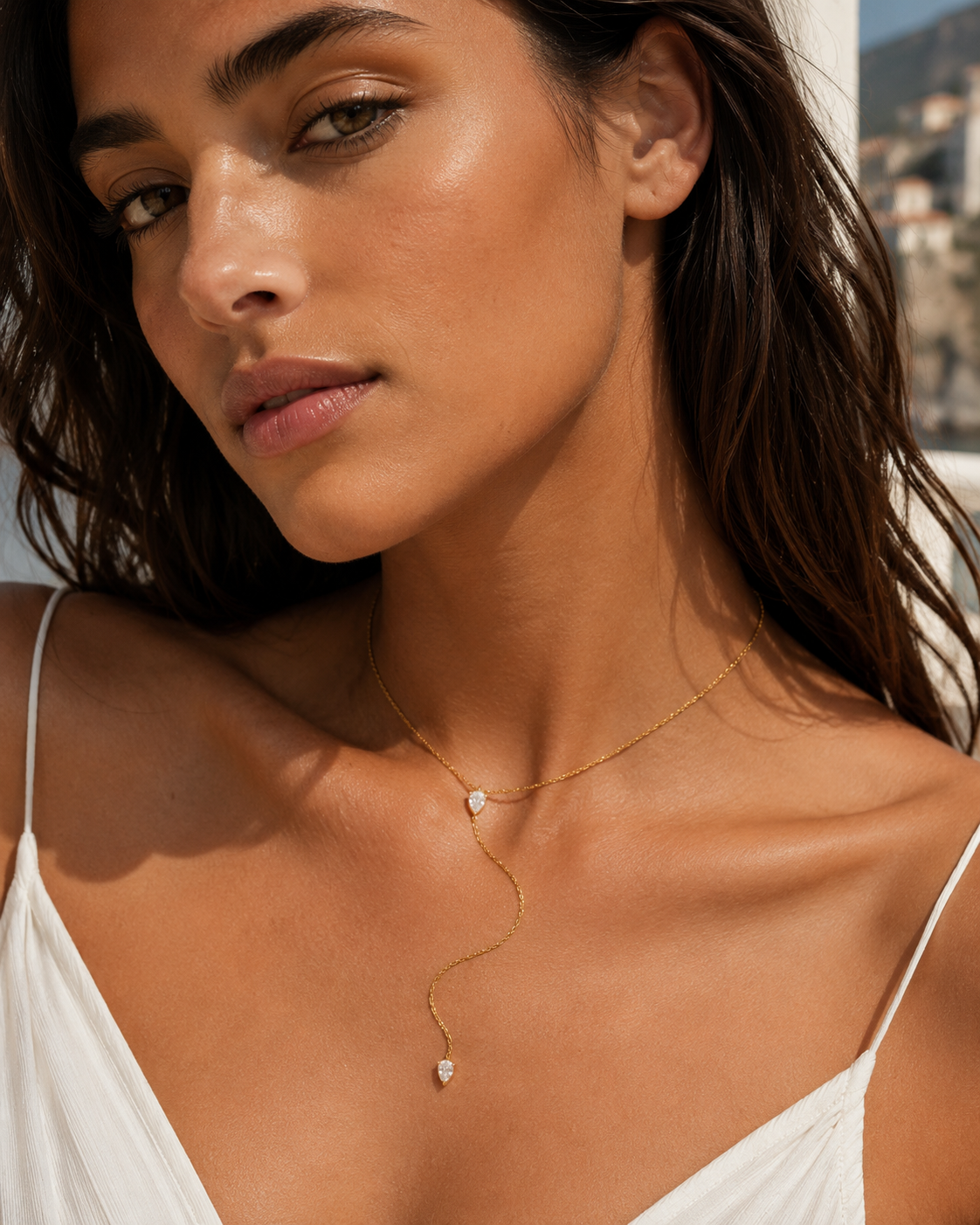 Model wears the gold Lariat Y NECKLACE with its pear-shaped crystal drop close to the neckline, in a sunlit portrait.