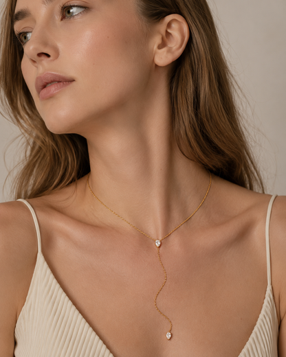 Model wears the gold Lariat Y NECKLACE with its crystal drop resting at the neckline, paired with a cream ribbed top.
