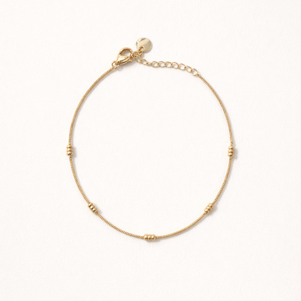 Lay Low BRACELET gold delicate chain bracelet with small ridged station beads, studio flat-lay on cream.