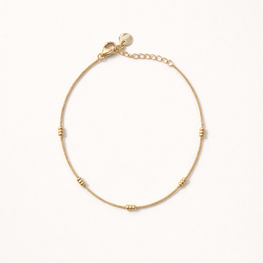 Lay Low BRACELET gold delicate chain bracelet with small ridged station beads, studio flat-lay on cream.