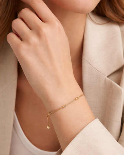 Lay Low BRACELET worn in gold on the wrist, close-up with a beige blazer and hand near the collarbone.