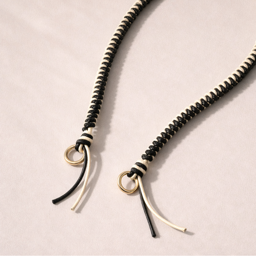Black and white two-tone braided Layover strap, close-up of the knotted gold ring and fringe end.