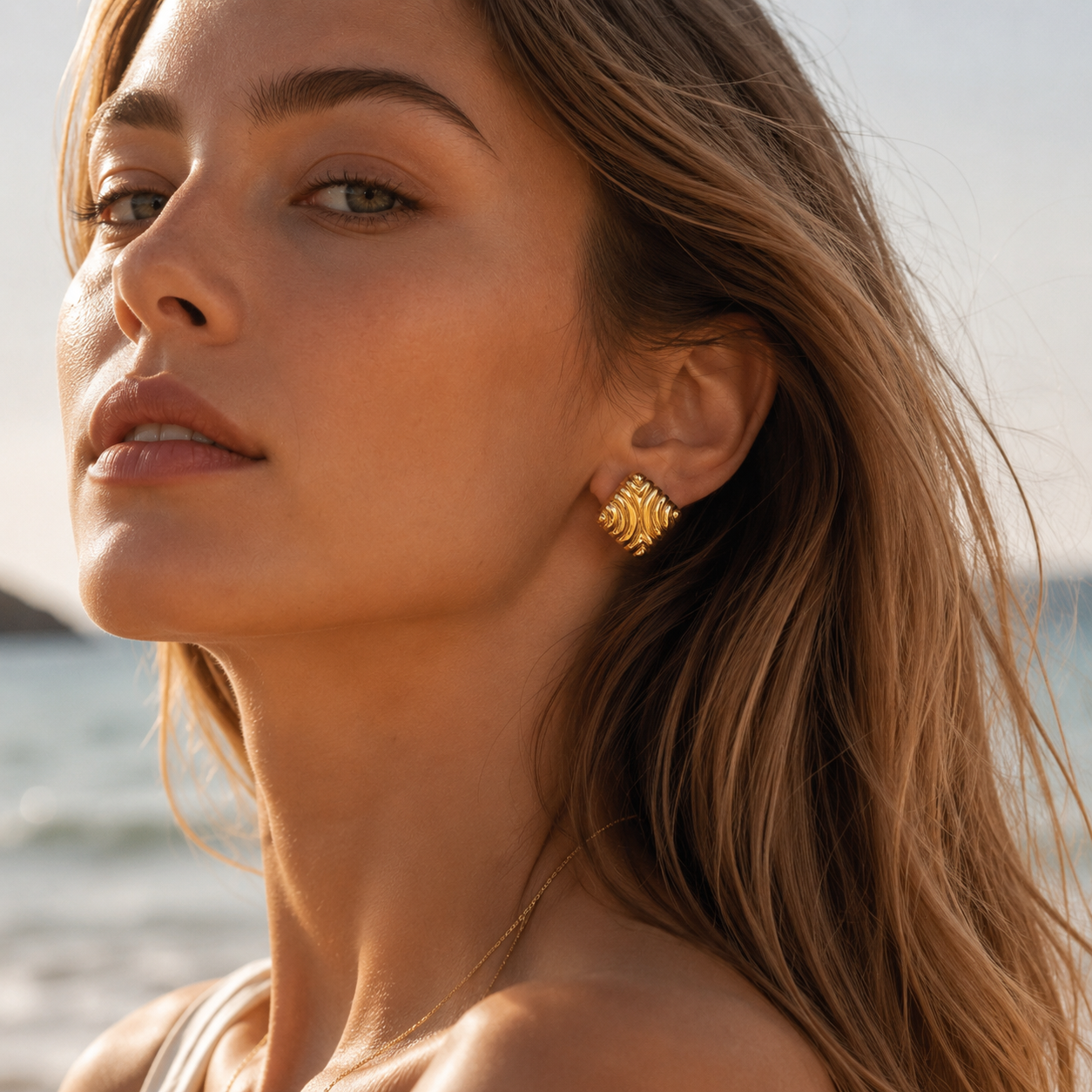 A model wears a gold Leia EARRINGS square stud with a swirling, ribbed wave texture and polished finish on her ear.
