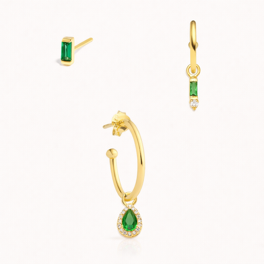The Leila SET in gold with emerald green stones, featuring a baguette stud, a baguette hoop, and a pear pavé halo dangle hoop in studio.