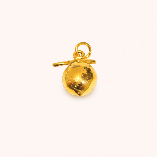 The Lemon CHARM in a studio flat lay, a polished gold pendant with a dimpled lemon texture and small stem on a cream background.