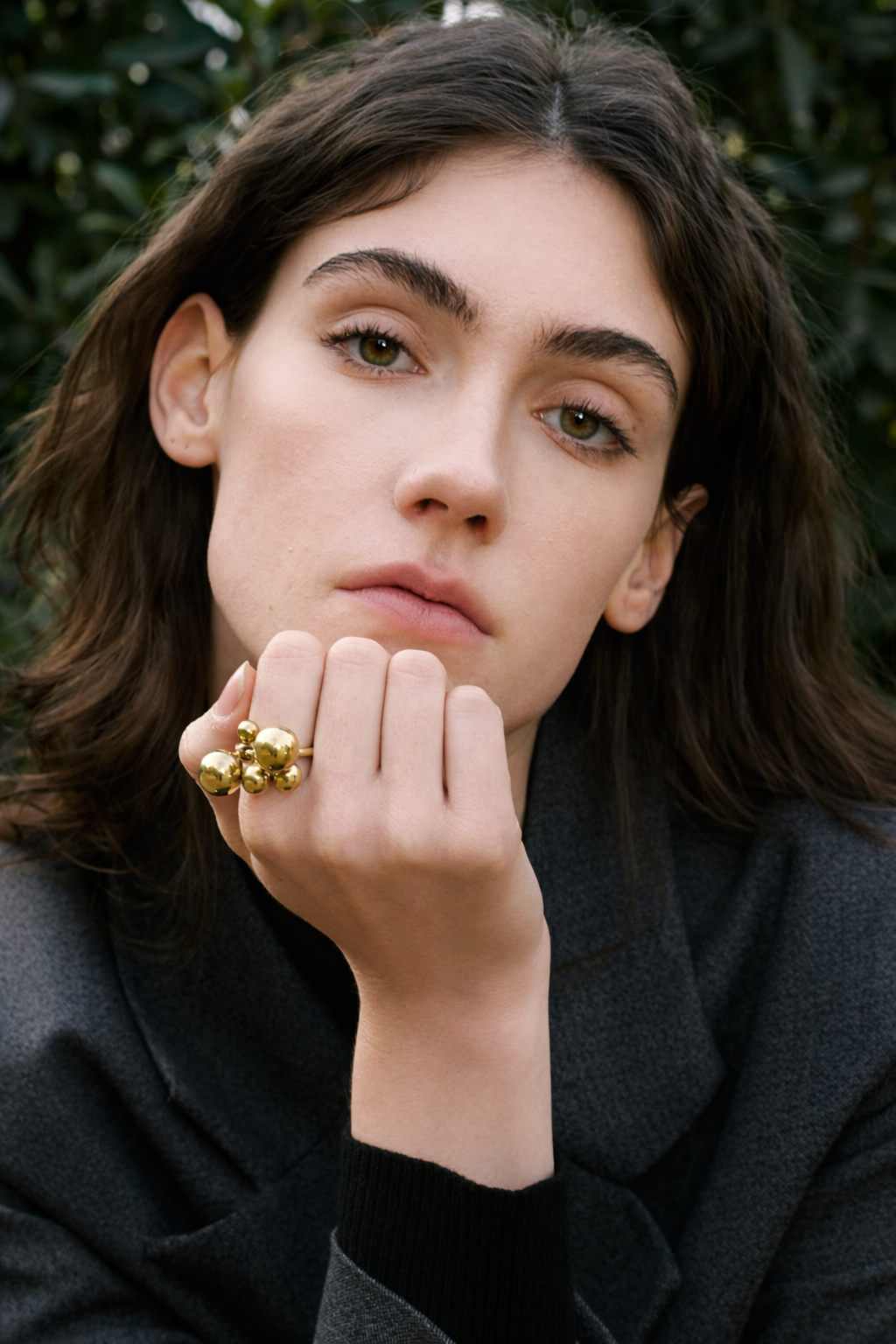 Close-up of a woman resting her chin on her hand, wearing the gold Lennox RING with its cluster of ball charms.