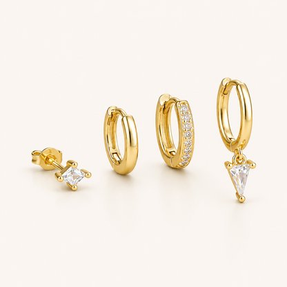Lexi Set of gold jewelry, a princess-cut stud, a plain hoop, a pave hoop, and a hoop with a triangle crystal drop, laid flat.