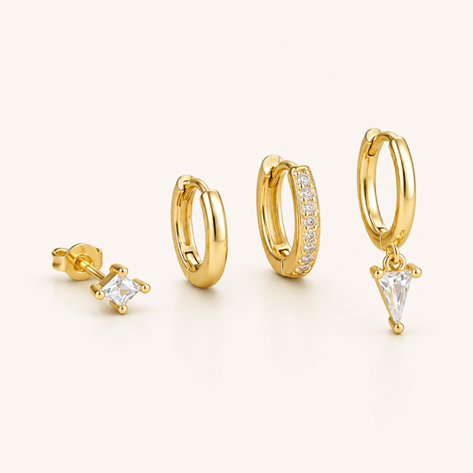 Lexi Set of gold jewelry, a princess-cut stud, a plain hoop, a pave hoop, and a hoop with a triangle crystal drop, laid flat.