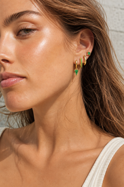 Lexi Set worn on the ear in green, a princess-cut stud stacked with hoops and a dangling green triangle crystal drop.
