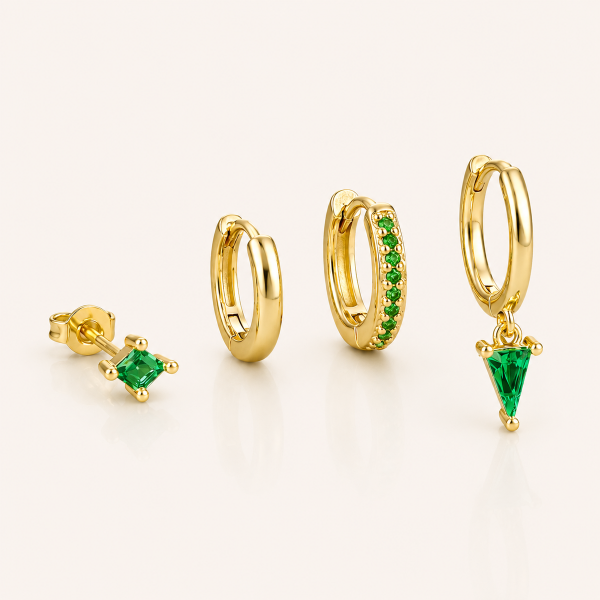 Lexi Set in green, a princess-cut stud, a plain hoop, a pave hoop, and a hoop with a green triangle crystal drop, laid flat.