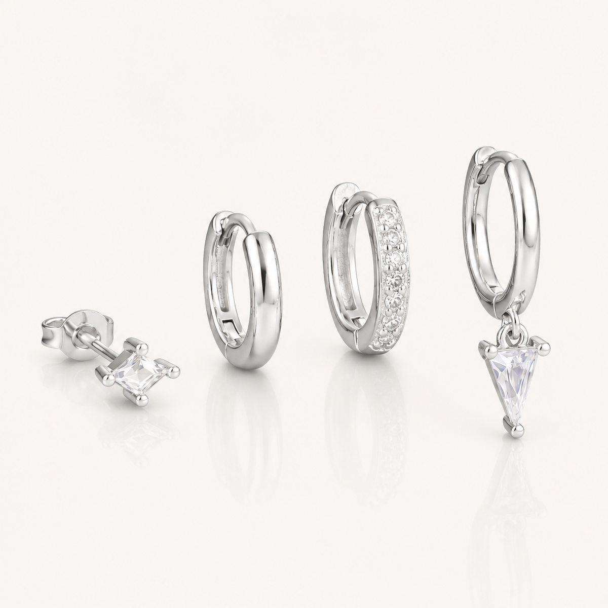 Lexi Set in silver tone, a princess-cut stud, a plain hoop, a pave hoop, and a hoop with a triangle crystal drop, laid flat.