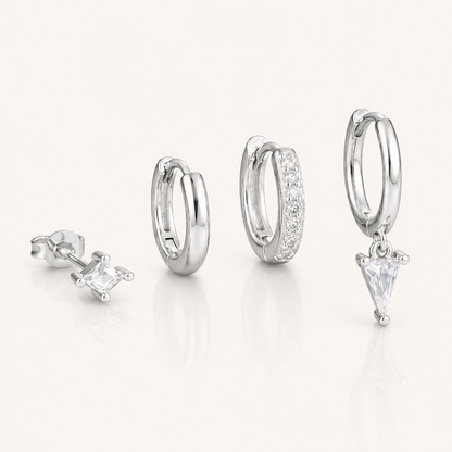 Lexi Set in silver tone, a princess-cut stud, a plain hoop, a pave hoop, and a hoop with a triangle crystal drop, laid flat.