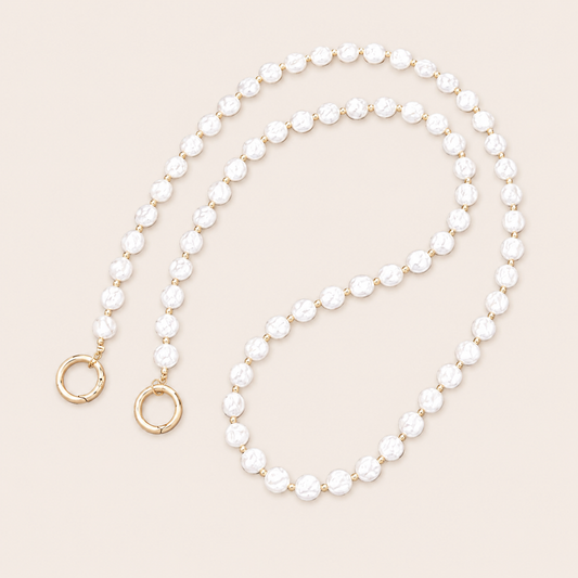 Folie à Trois Linden Pearl wholesale phone chain in textured white pearls with gold spacer beads and gold ring clasps, coiled on a cream background.