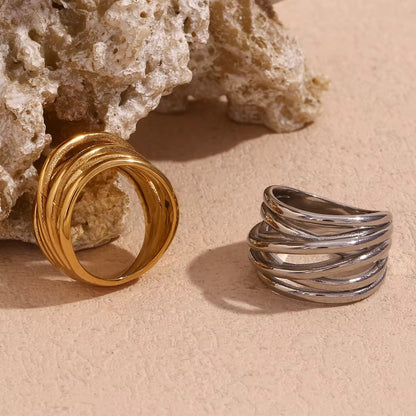 Gold and silver wide wrap-style Lizie RING pieces propped against a textured stone, layered wire bands visible.