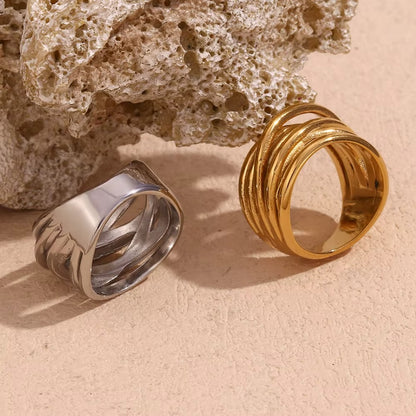 Wide silver band Lizie RING beside its gold wrap-style counterpart, both resting against a textured stone.