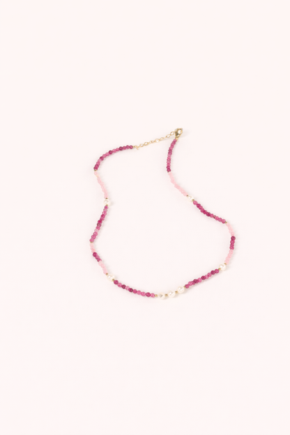 The Lolita NECKLACE, a beaded strand of pink and burgundy gemstones interspersed with small pearls, shown flat.
