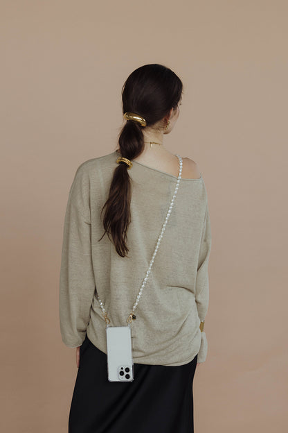 Woman seen from behind wearing a long round pearl Long Pearl PHONE STRAP crossbody with her phone, olive sweater, black skirt.