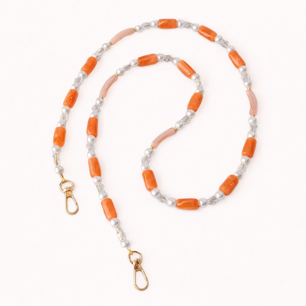 Coral and pink beaded Loreto phone strap coiled flat, finished with pearl and crystal accents.