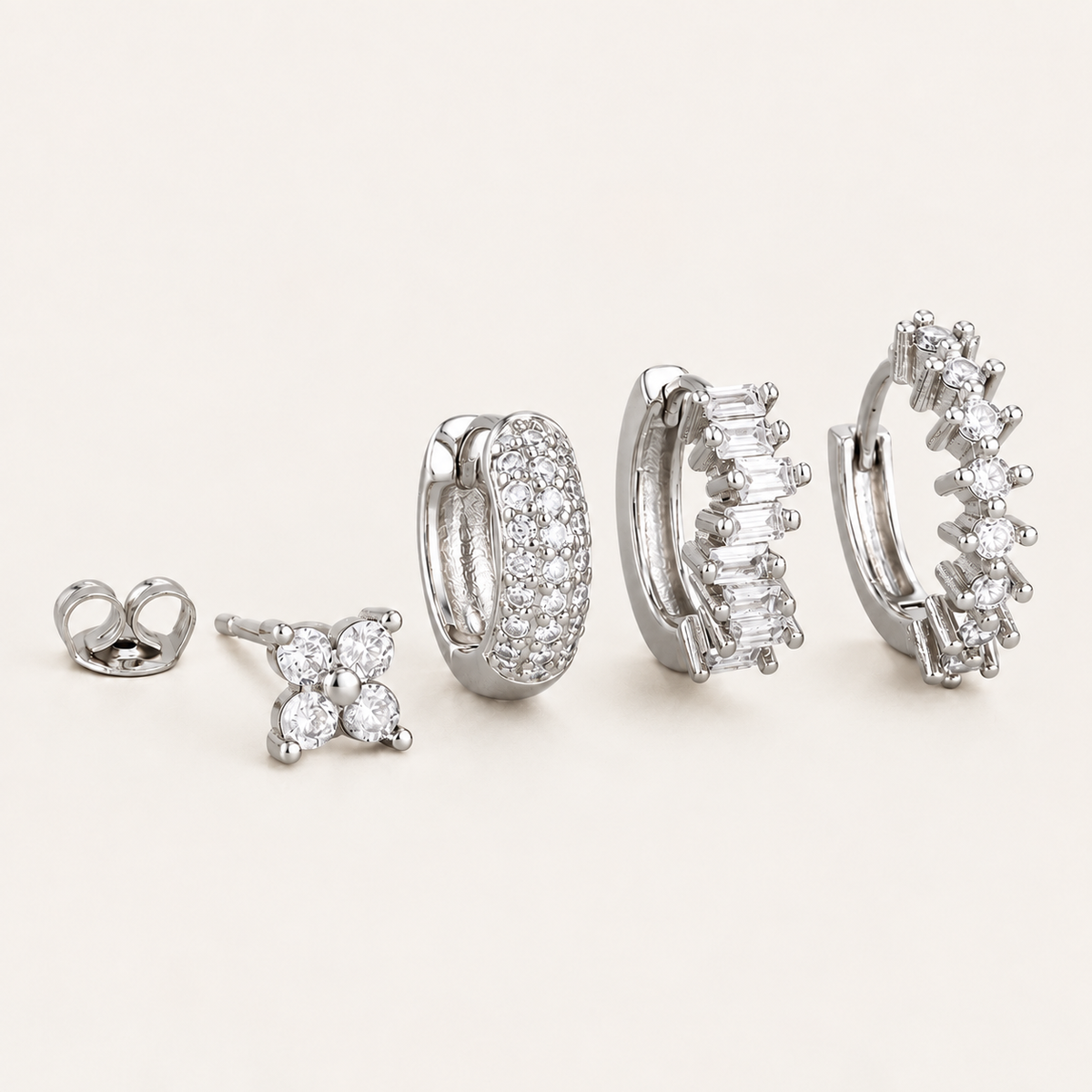 The Folie à Trois Lou SET in silver: a four-stone flower stud, a pavé hoop, a baguette-stone hoop and a round-stone hoop.