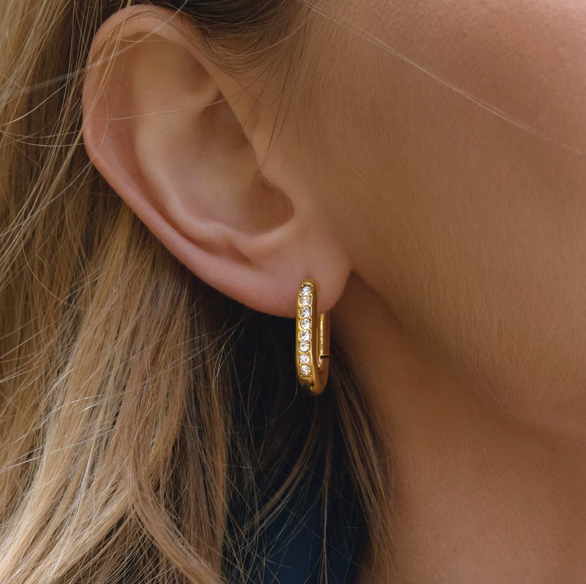 Worn on a model's ear, the Love Bite EARRINGS show their pave crystal-lined rectangular hoop shape up close.