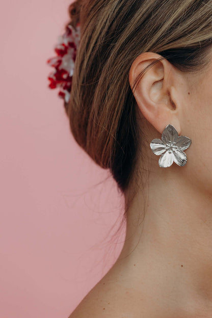 Styled with an updo, Love Language Earrings show their silver flower stud catching the light near the ear.