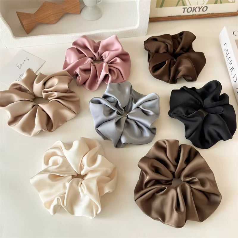 Lucia SCRUNCHIE XL flat-lay of seven colors including mauve, brown, taupe, grey, black, cream and olive, styled with books.