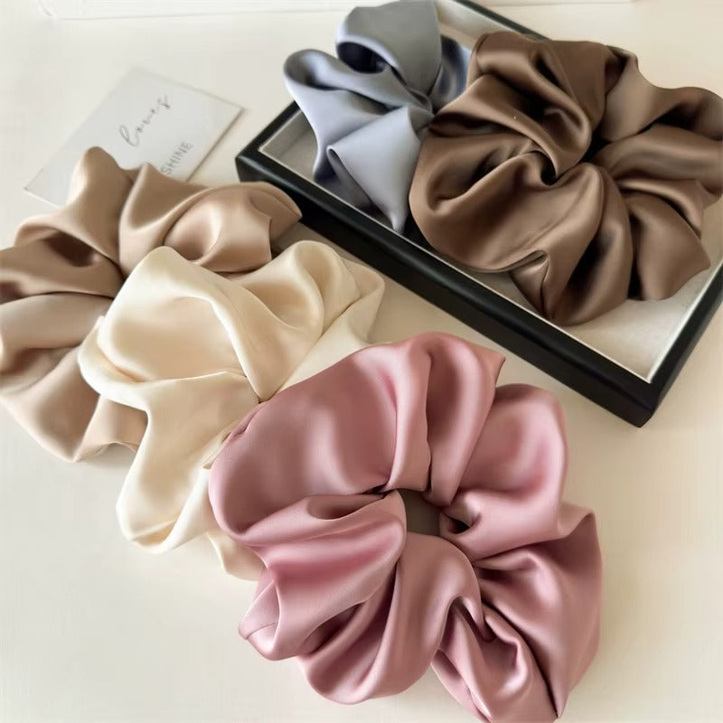 Lucia SCRUNCHIE XL flat-lay of four colors in a gift box: grey, olive taupe, cream and mauve satin scrunchies.
