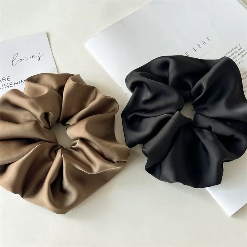 Lucia SCRUNCHIE XL two oversized satin scrunchies side by side in olive taupe and black, on magazine pages.